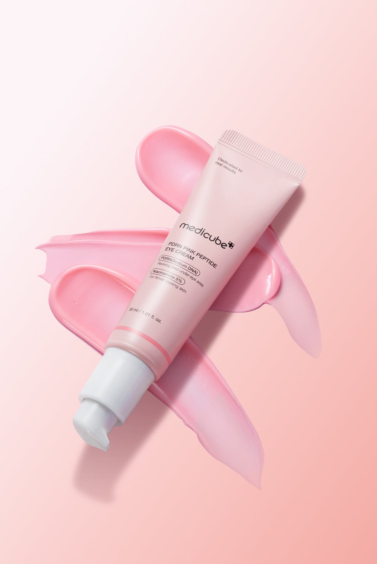 A pink PDRN eye cream tube resting on swatches of pink cream